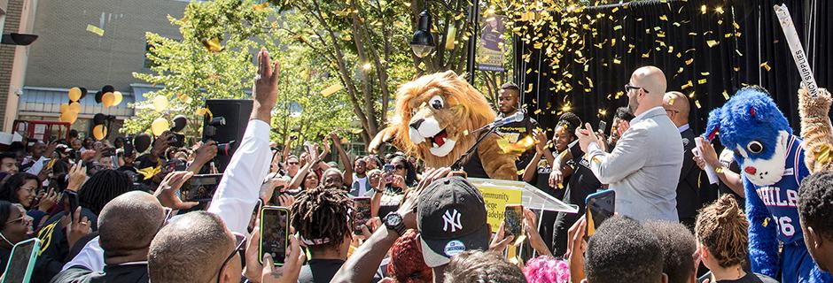 Roary on stage on 17th street with confetti flying around and everyone in the crowd is cheering. 