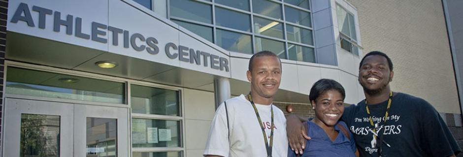 Three students posing for a photo in front of the entrance to the athletics center. 