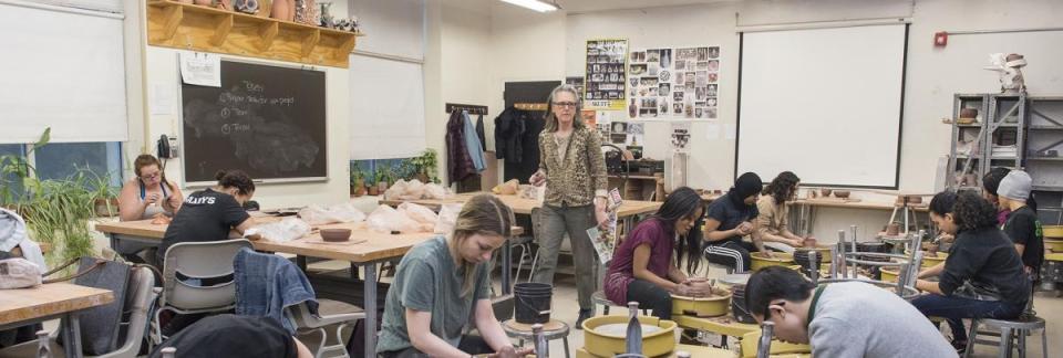 Teacher walking throughout the classroom while ceramics students are busy throwing pottery